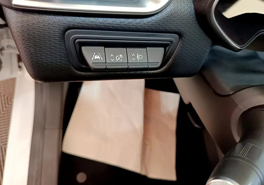 Gros plan sur les commandes d'assistance à la conduite sous le tableau de bord d'une Renault Clio blanche.
