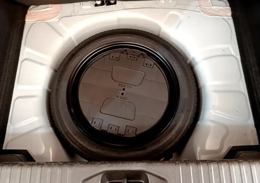 Vue plongeante sur la roue de secours noire dans le coffre blanc d'une Renault Clio Business Blue dCi 85 2020.