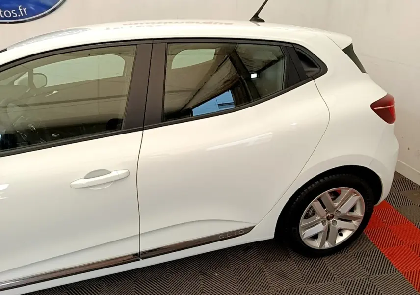 Vue latérale côté droit d'une Renault Clio blanche Business Blue dCi 85 avec jantes alliage et logo Clio sur la bas de caisse.