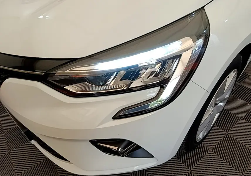 Gros plan sur l'avant droit blanc d'une Renault Clio 2020 avec phares LED allumés et jante visible.