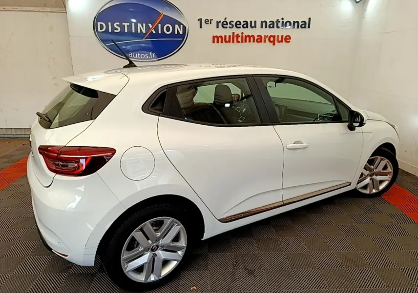 Vue 3/4 arrière droite d'une Renault Clio Business Blue dCi 85 blanche avec jantes alliage et logo Distinxion en arrière-plan.
