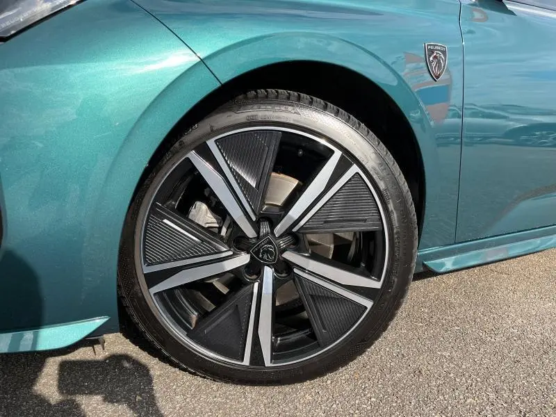 Gros plan sur la roue avant droite et l'aile bleu Avatar d'une Peugeot 308 SW 2023 avec logo lion noir brillant.