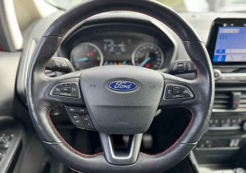 Volant en cuir perforé noir avec surpiqûres rouges du Ford Ecosport ST-Line, tableau de bord et écran tactile en arrière-plan.