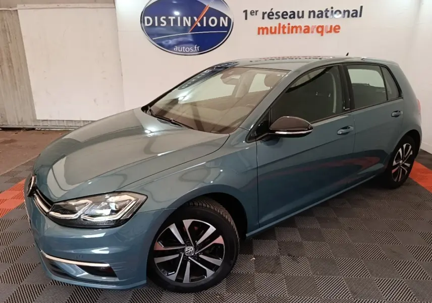 Volkswagen Golf bleu vue 3/4 avant droit, avec jantes noires et phares LED dans un showroom intérieur.