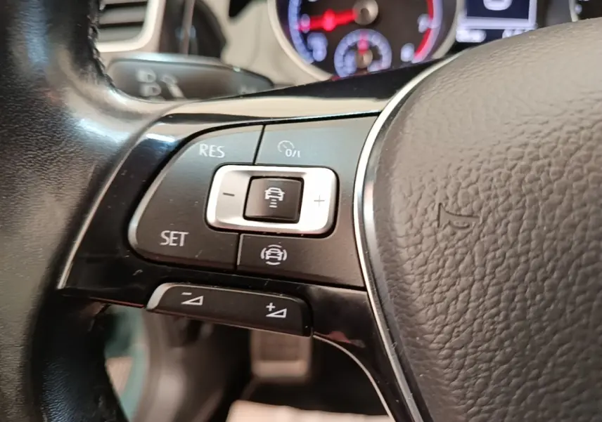 Gros plan sur le volant cuir multifonctions de la Volkswagen Golf bleu, avec commandes de régulateur de vitesse.