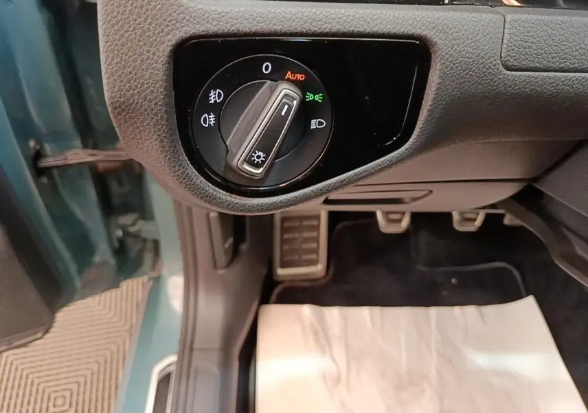 Gros plan sur le bouton de commande des phares à gauche du volant dans une Volkswagen Golf bleu, intérieur côté conducteur.
