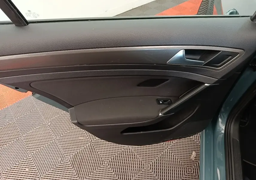 Vue intérieure de la porte avant gauche d’une Volkswagen Golf bleu 2020, avec panneau noir et poignée argentée.