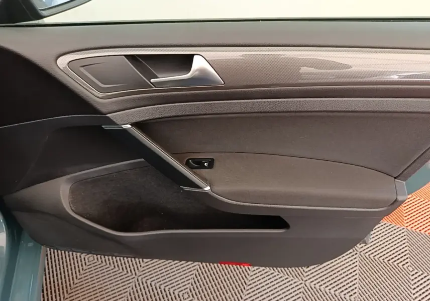 Vue rapprochée de la porte intérieure côté gauche d’une Volkswagen Golf 1.0 TSI 115 BVM6 IQ.DRIVE avec garniture noire et insert décoratif gris.