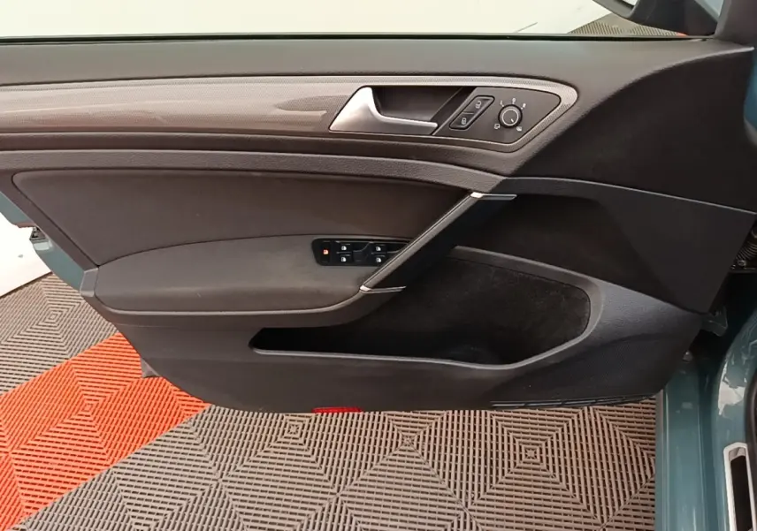 Vue intérieure côté gauche de la porte avant d’une Volkswagen Golf bleu, avec commandes électriques et poignée argentée.
