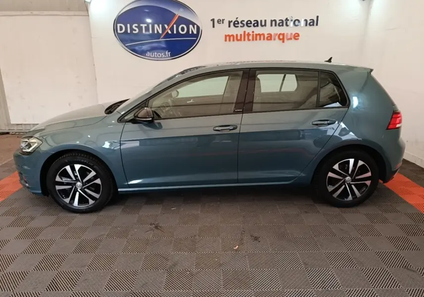 Profil latéral gauche d'une Volkswagen Golf bleu 2020 avec jantes alliage et vitres teintées en intérieur showroom.