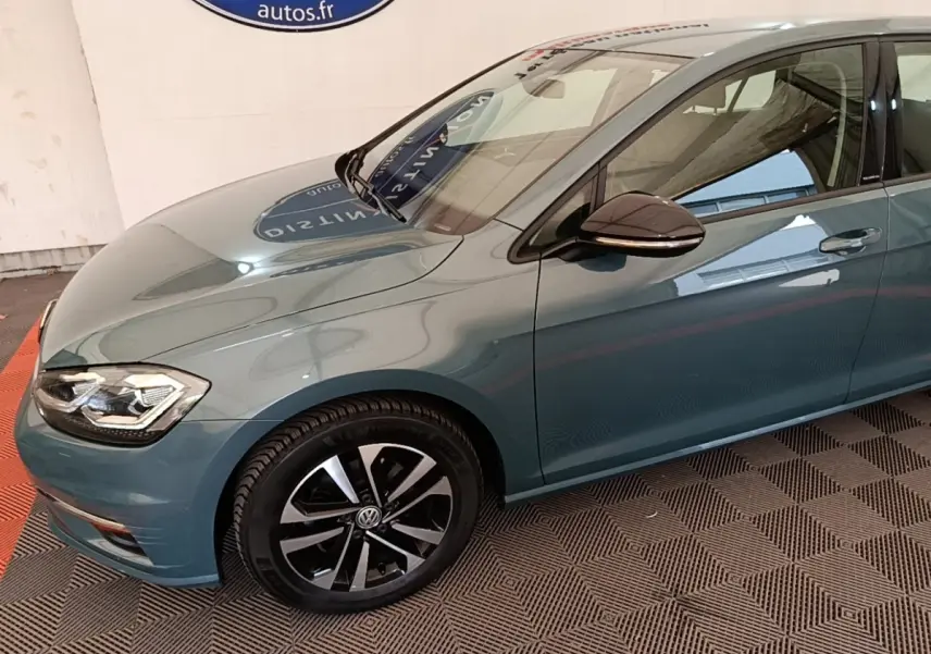 Vue 3/4 avant droit d’une Volkswagen Golf bleu métallisé avec jantes alliage noires et rétroviseur ton caisse.