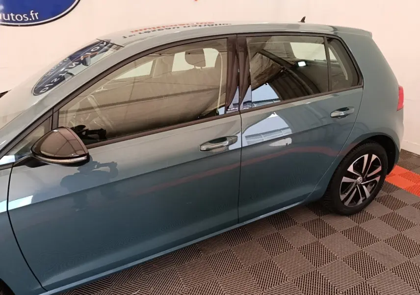 Vue latérale gauche d'une Volkswagen Golf bleu métallisé avec jantes alliage et rétroviseur noir.