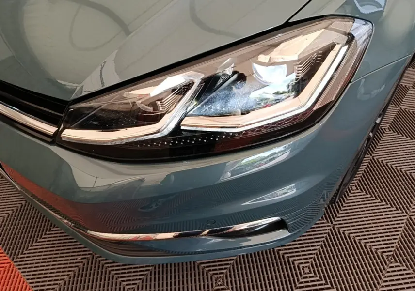 Gros plan sur le phare avant droit d’une Volkswagen Golf bleu 2020 avec détails LED et pare-chocs chromé.