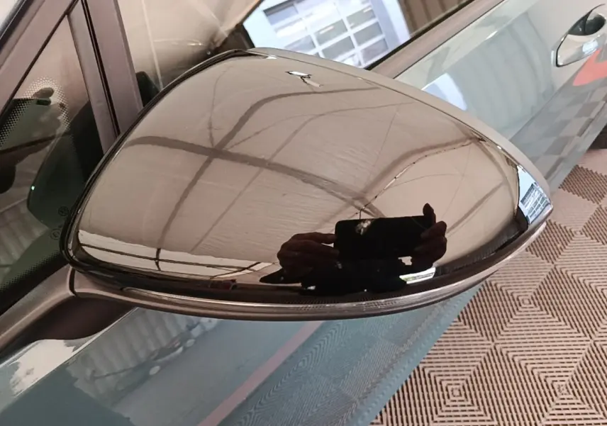 Rétroviseur droit chromé d'une Volkswagen Golf bleu, vue rapprochée avec reflet du plafond et main.