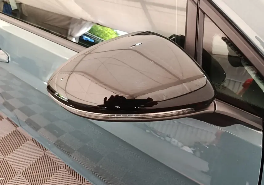 Rétroviseur extérieur noir en gros plan sur la porte côté gauche d’une Volkswagen Golf bleu clair.