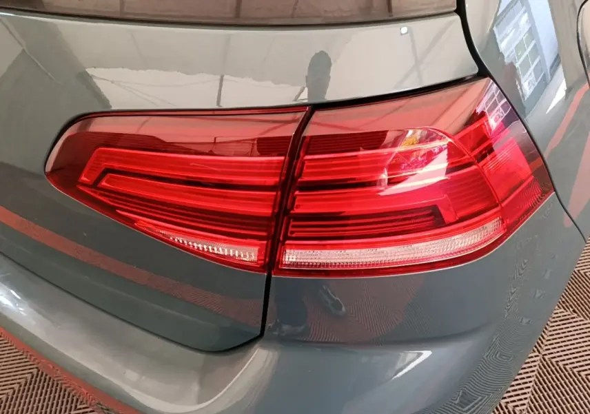 Gros plan sur le feu arrière droit rouge d’une Volkswagen Golf bleu foncé, avec reflet sur la carrosserie.