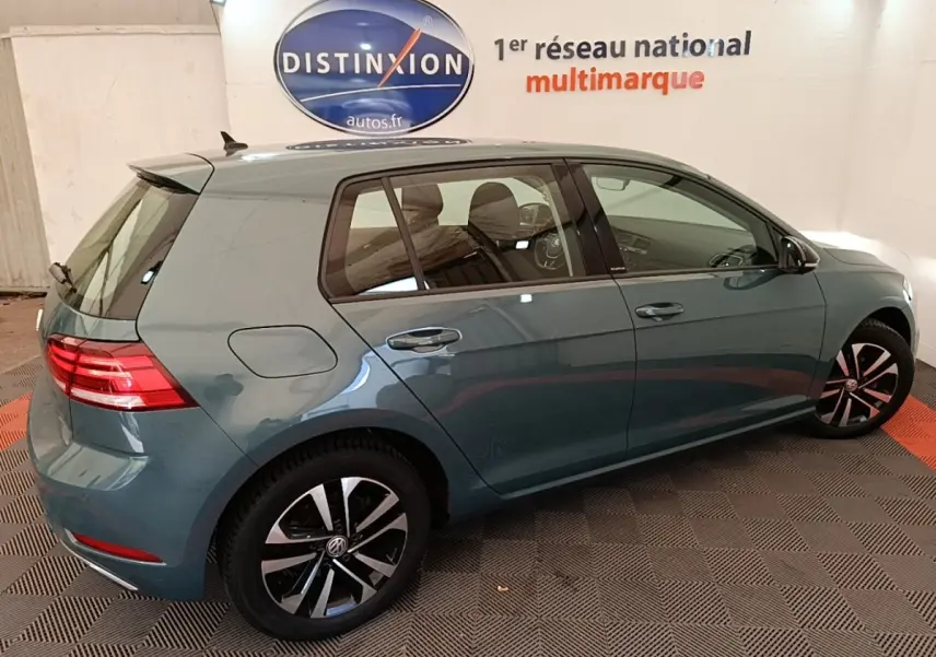 Vue 3/4 arrière droite d'une Volkswagen Golf bleu métallisé, avec jantes alliage et feux arrière LED allumés.