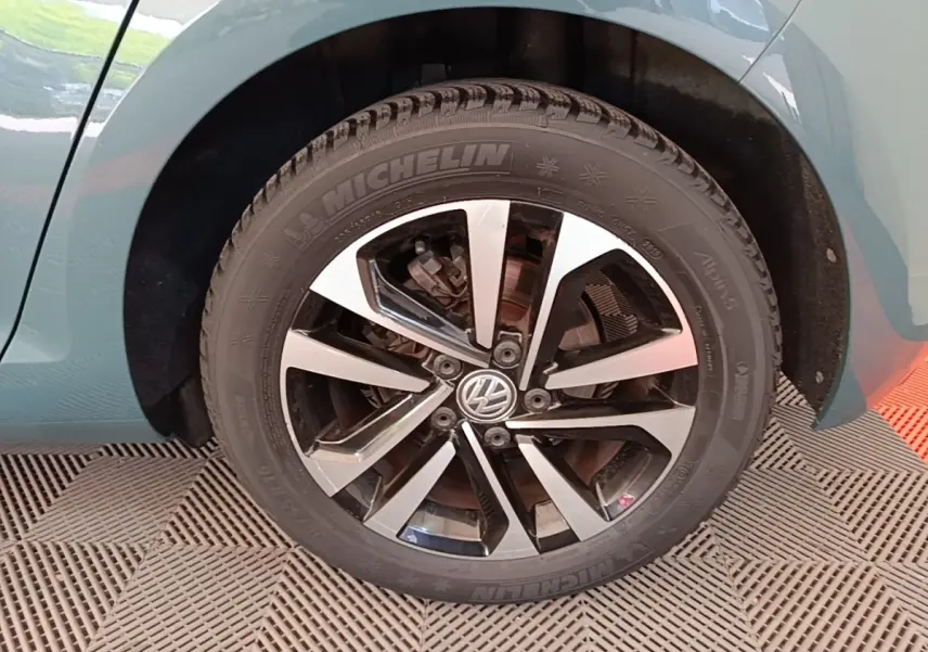 Gros plan sur la roue avant gauche d'une Volkswagen Golf bleue, jante alliage bicolore avec logo VW central.
