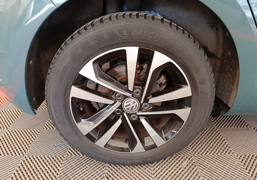 Gros plan sur la roue avant gauche d'une Volkswagen Golf bleue, mettant en valeur la jante alliage bicolore et le pneu hiver.