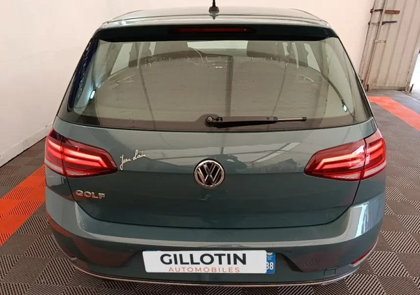 Vue arrière d'une Volkswagen Golf bleu foncé avec feux LED et logo VW visible dans un garage.