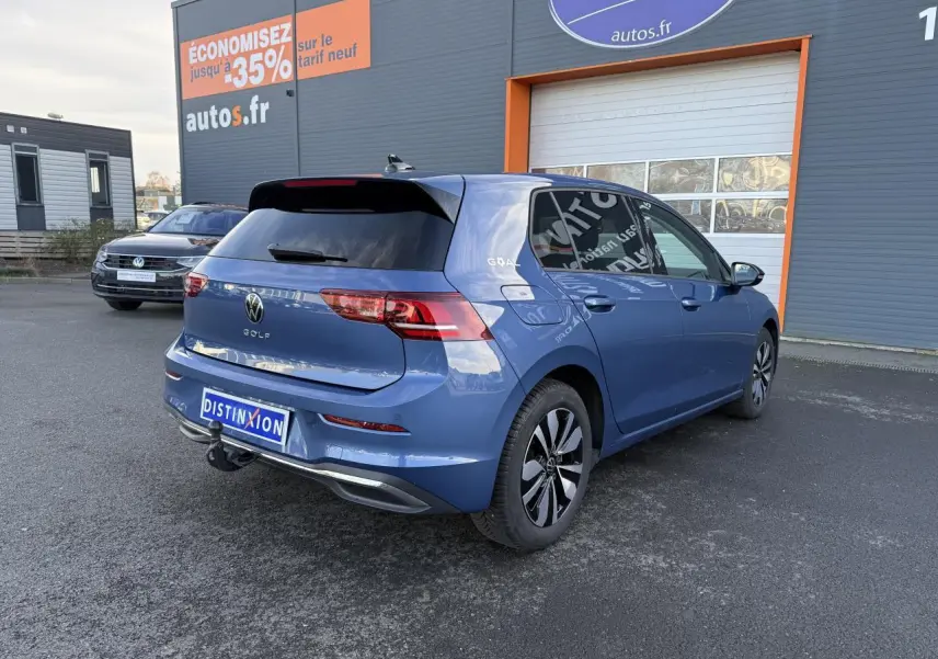 Volkswagen Golf 2025 bleu métallisé en 3/4 arrière droit avec attelage escamotable et vitres arrière surteintées.