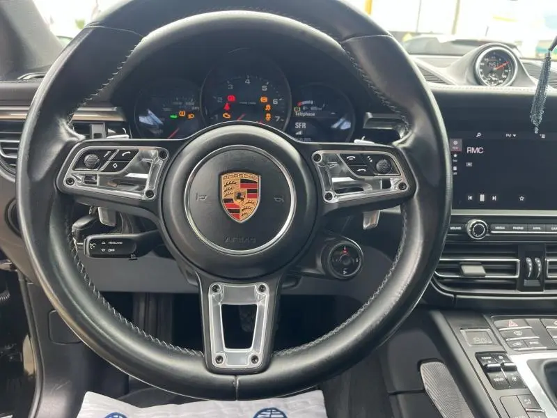 Vue rapprochée du volant cuir noir de la Porsche Macan 2.0 245ch avec tableau de bord et écran tactile visibles
