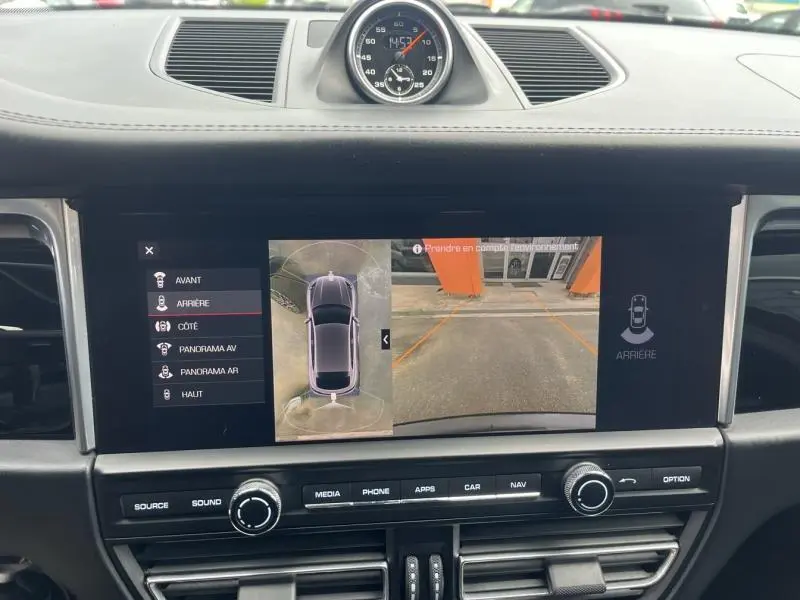 Vue intérieure du tableau de bord du Porsche Macan noir 2018 avec écran multimédia affichant la caméra de recul et l'horloge centrale analogique.