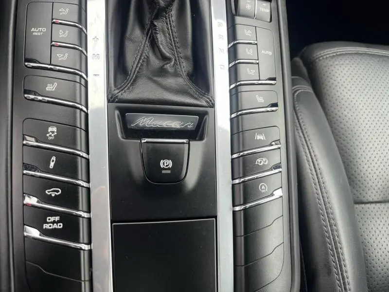 Gros plan sur la console centrale noire du Porsche Macan 2.0 avec levier PDK en cuir et boutons de contrôle argentés.