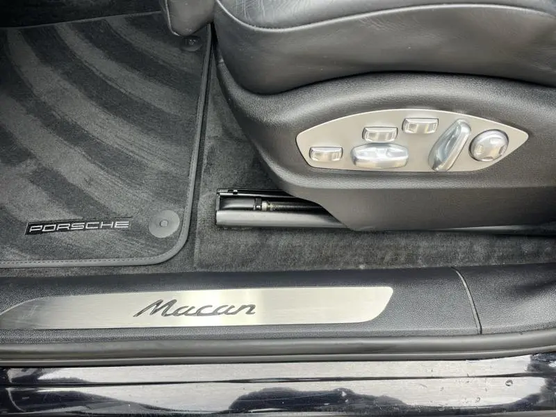 Détail de la commande électrique du siège et seuil de porte Macan sur tapis noir d'un Porsche Macan noir 2018