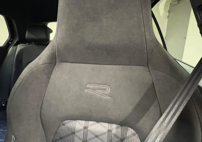 Gros plan sur le siège avant en alcantara gris foncé avec logo R, ceinture de sécurité visible à droite.