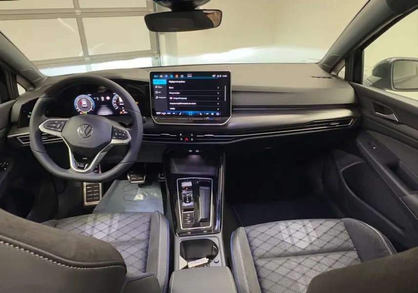 Vue intérieure avant de la Volkswagen Golf 2.0 TDI R-Line 2026, avec tableau de bord moderne et sièges tissu noir à motifs.