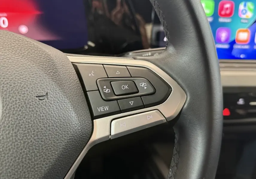 Gros plan sur le volant cuir noir de la Volkswagen Golf 2.0 TDI, avec commandes multifonctions et écran tactile en arrière-plan.