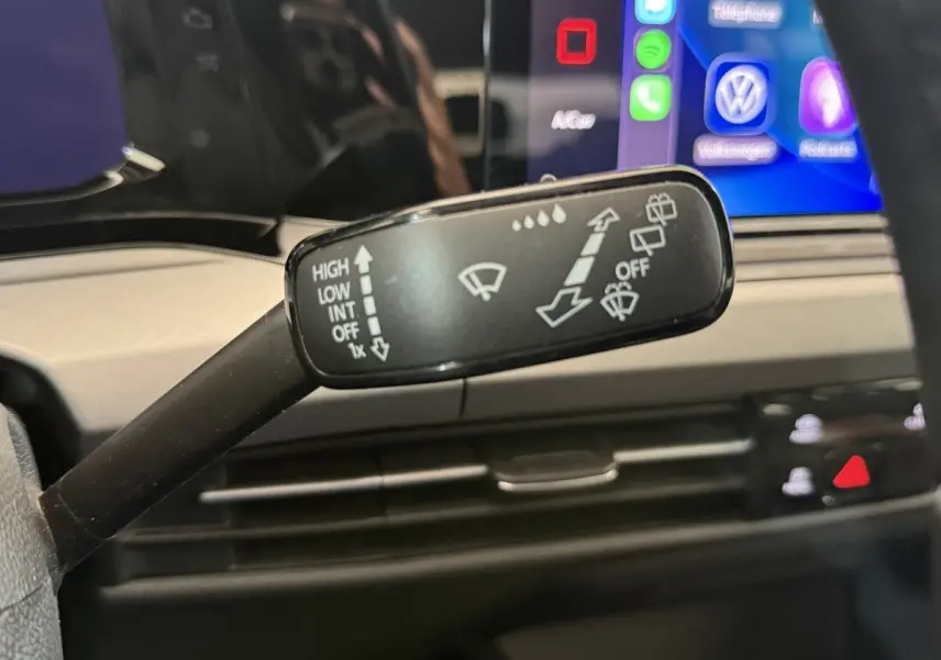 Gros plan sur la commande des essuie-glaces dans l’habitacle d’une Volkswagen Golf bleu, avec écran tactile en arrière-plan.