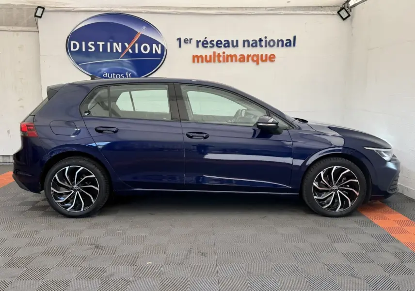 Profil droit d'une Volkswagen Golf bleu foncé 2021 avec jantes alliage noires et détails argentés, en intérieur showroom.