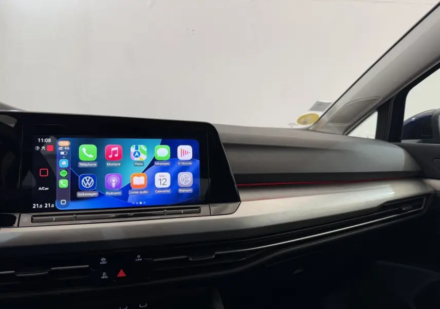 Vue intérieure côté passager du tableau de bord de la Volkswagen Golf bleu, avec écran tactile et bandeau lumineux rouge.