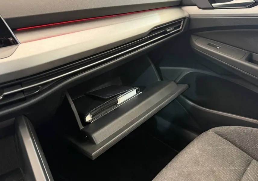 Intérieur Volkswagen Golf 2.0 TDI 2021, vue sur boîte à gants ouverte avec livret, tableau de bord noir et garniture claire.