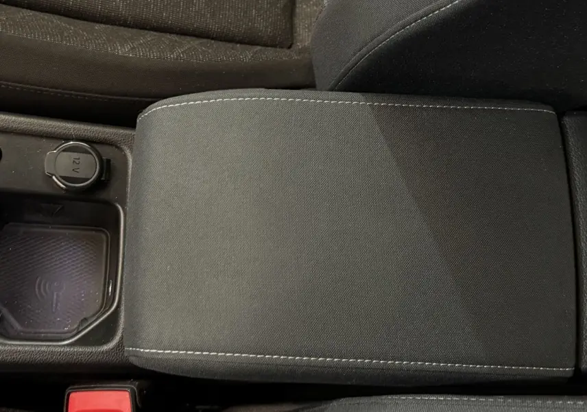 Gros plan sur l'accoudoir central noir et la prise 12V avec zone de recharge à induction dans une Volkswagen Golf bleue.