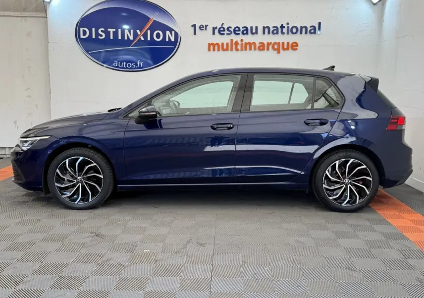 Profil côté gauche d'une Volkswagen Golf 2.0 TDI bleu foncé avec jantes alliage noires et argentées, en intérieur showroom.