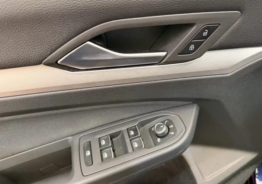 Gros plan sur la porte côté conducteur de la Volkswagen Golf bleu, montrant les commandes des vitres et le bouton de verrouillage.
