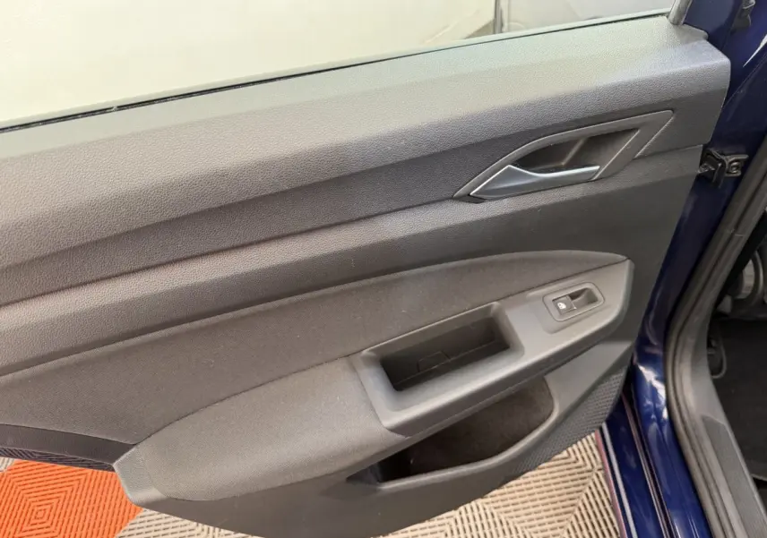 Vue rapprochée de la porte avant gauche bleu foncé d'une Volkswagen Golf 2021, avec poignée intérieure grise.