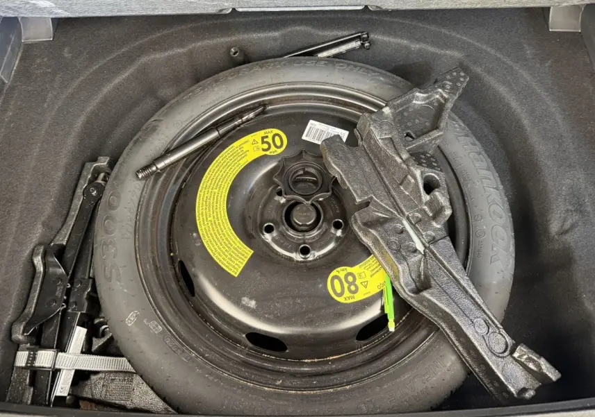 Vue rapprochée de la roue de secours noire et des outils dans le coffre d’une Volkswagen Golf bleu 2021.