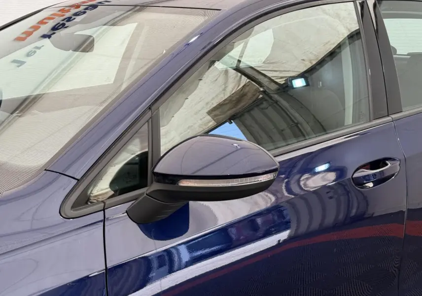 Vue rapprochée du côté gauche d'une Volkswagen Golf bleu métallisé, mettant en valeur le rétroviseur et la poignée de porte.