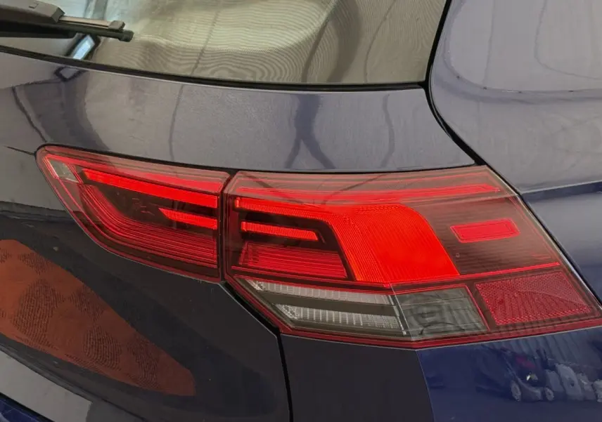 Feu arrière droit rouge et blanc sur Volkswagen Golf bleu, vue rapprochée du coin arrière du véhicule.