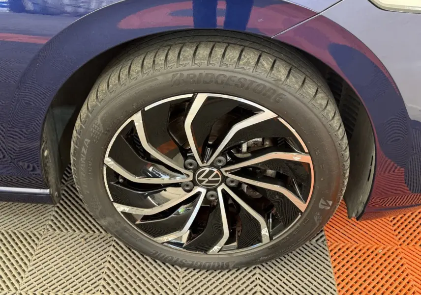 Gros plan sur la roue avant droite d’une Volkswagen Golf bleu, jante alliage noir et argentée au design dynamique.