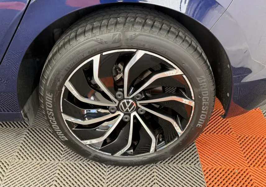 Gros plan sur la roue avant droite d'une Volkswagen Golf bleue, avec jante alliage noire et chromée distinctive.