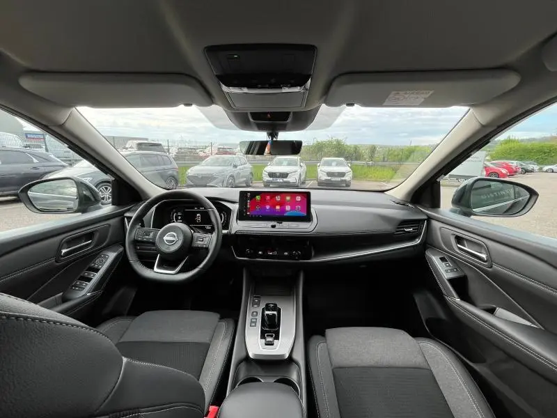 Vue intérieure avant du Nissan Qashqai e-POWER 2024, tableau de bord noir avec écran tactile central et volant multifonction cuir.
