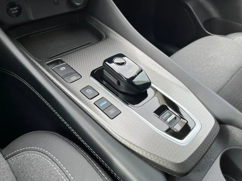 Vue rapprochée de la console centrale noire et grise du Nissan Qashqai e-POWER 2024 avec levier de vitesse électronique et boutons de mode de conduite.