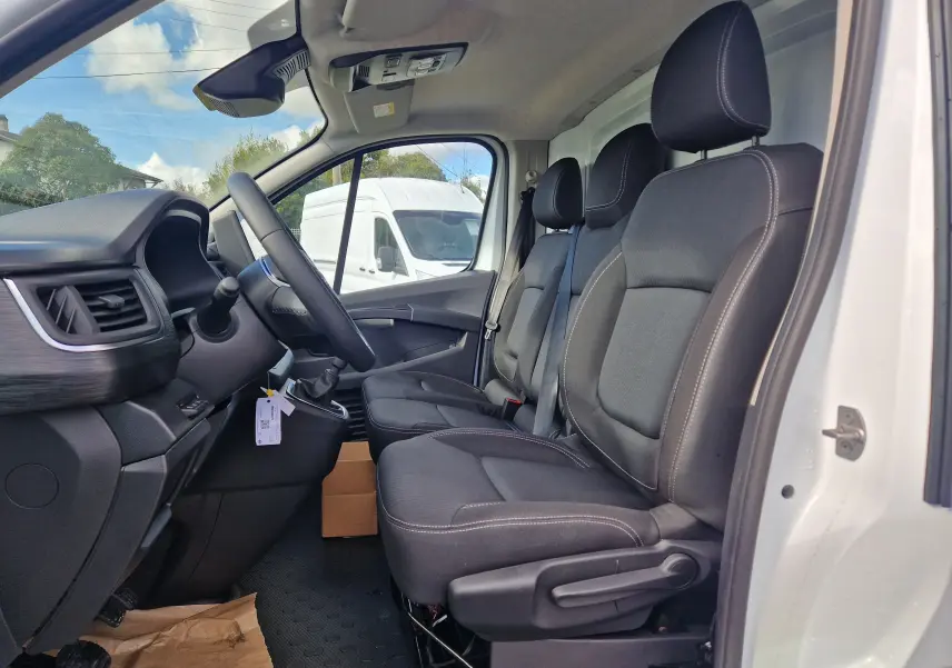 Vue intérieure côté conducteur du Nissan Primastar blanc 2025, montrant les sièges noirs et le tableau de bord avec volant.