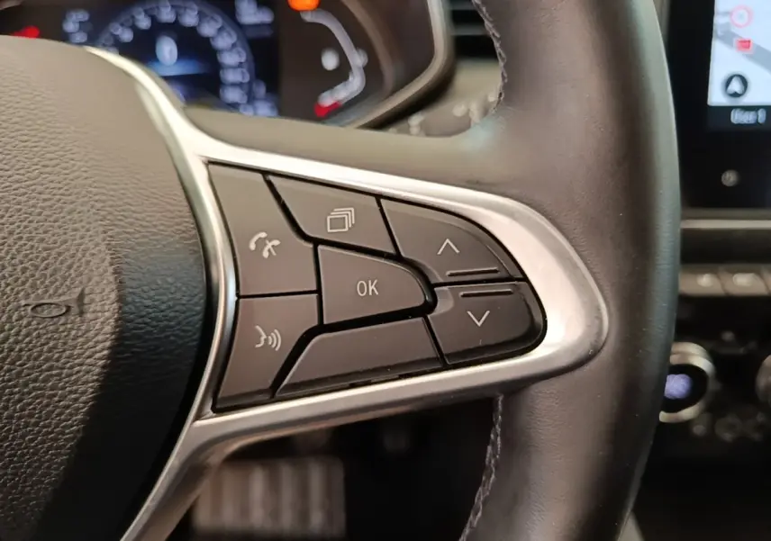 Gros plan sur les commandes multifonctions du volant cuir noir d’une Renault Clio Intens gris foncé, tableau de bord en arrière-plan.