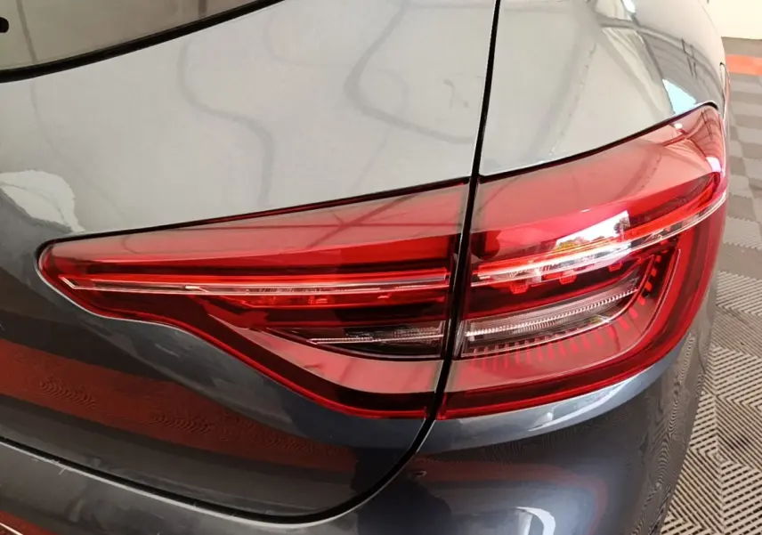 Gros plan sur le feu arrière droit rouge d'une Renault Clio Intens gris foncé, avec partie de la carrosserie visible.